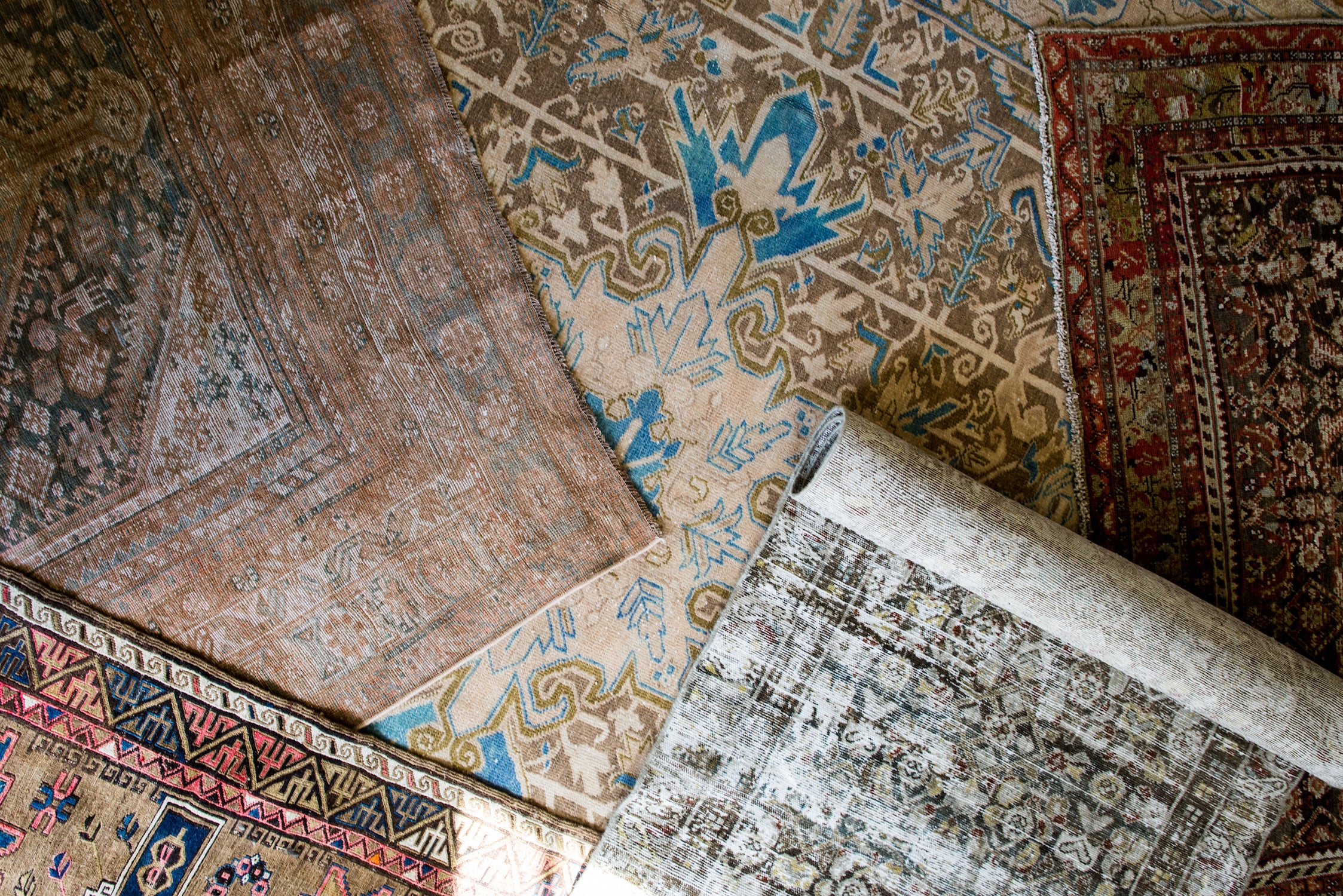 Home tests for rugs: folding to see knots, checking if fringe is part of the base, feeling wool’s warm texture, and noticing natural smell versus synthetic chemicals.