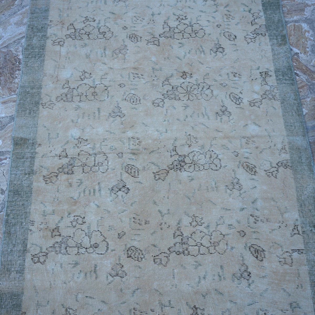 Close-up of the beige Turkish distressed vintage rug showing floral details, hand-knotted weave, wool and cotton and low pile.