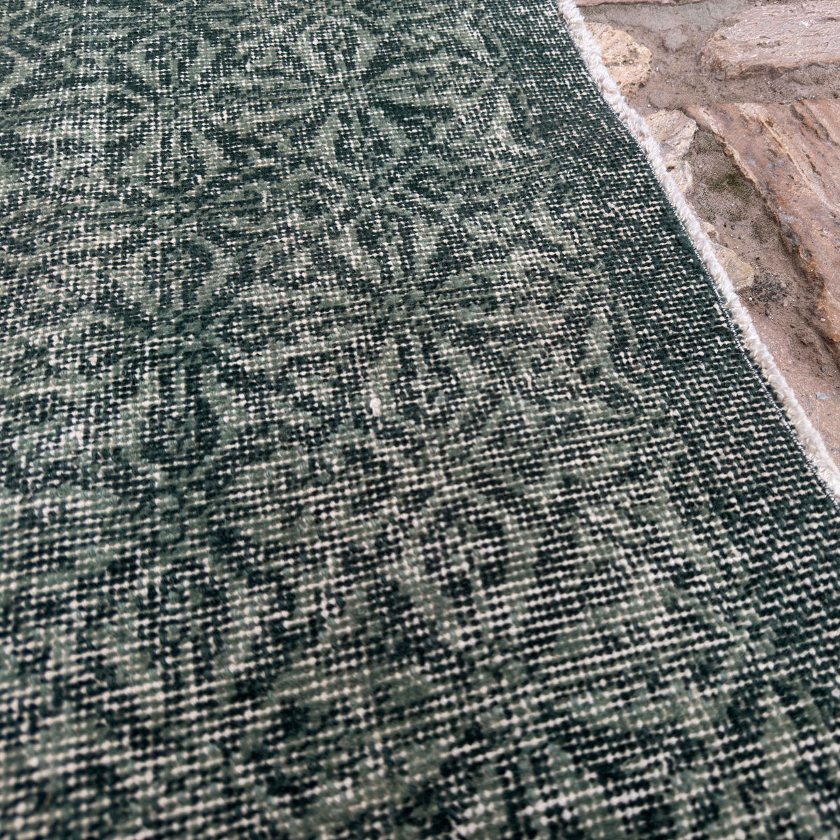 Close-up of the green geometric turkish rug showing floral details, hand-knotted weave, wool and cotton and low pile.