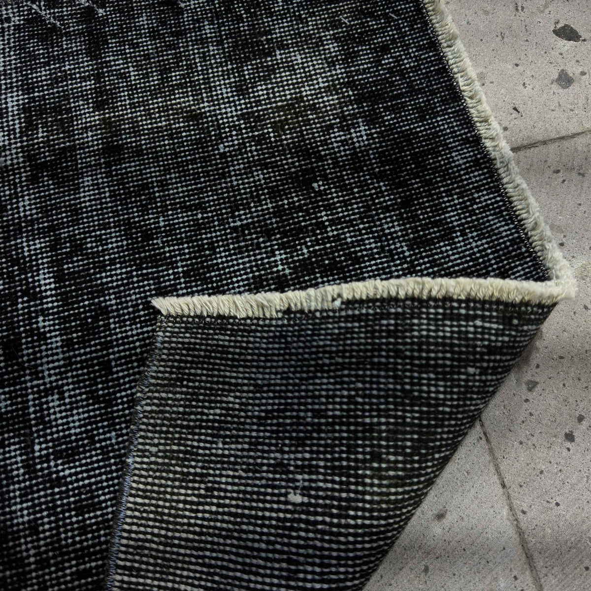 Close-up of the black Turkish mini overdyed rug showing overdyed details, hand-knotted weave, wool and cotton and low pile.