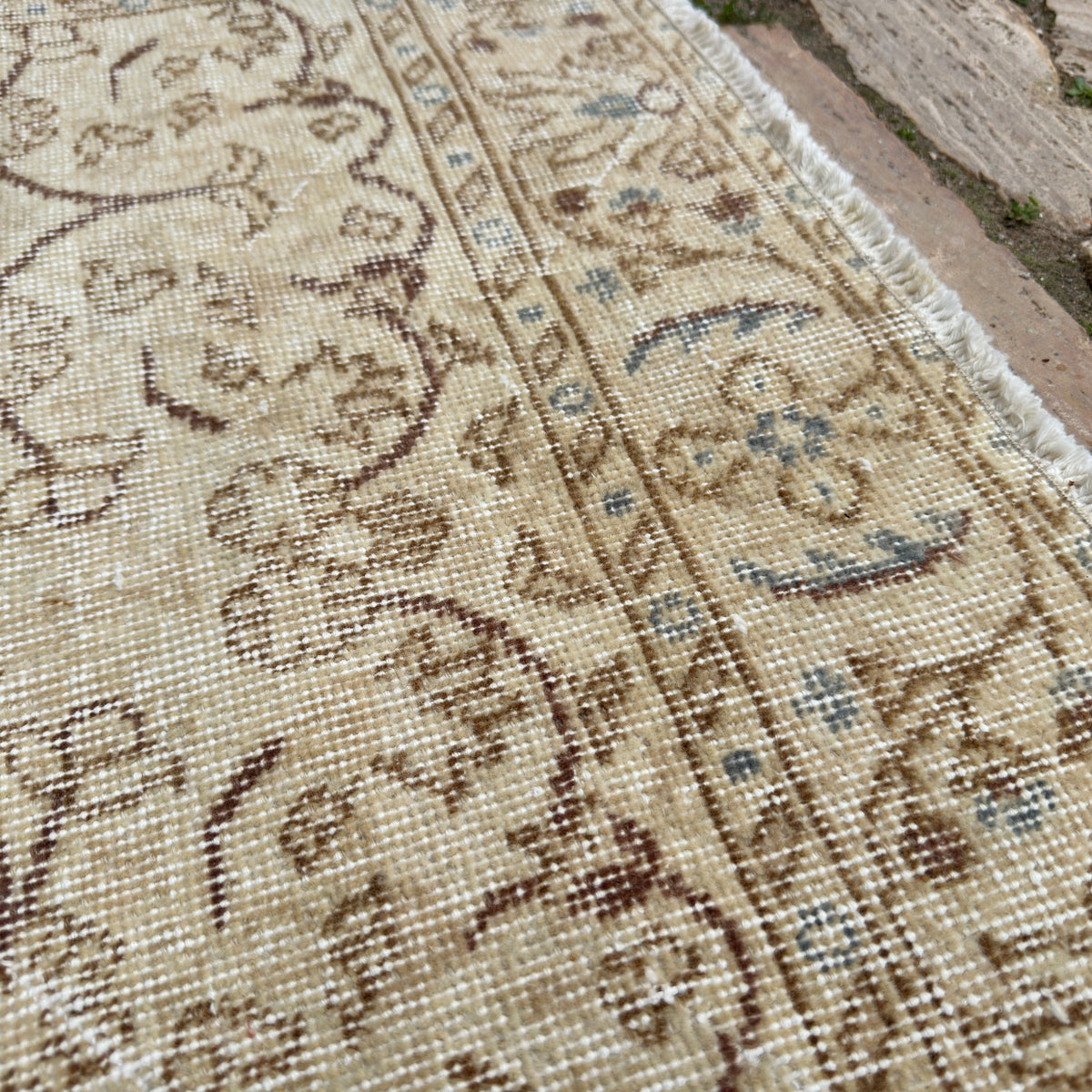 Close-up of the beige vintage Turkish area rug showing floral details, hand-knotted weave, wool and cotton and low pile.