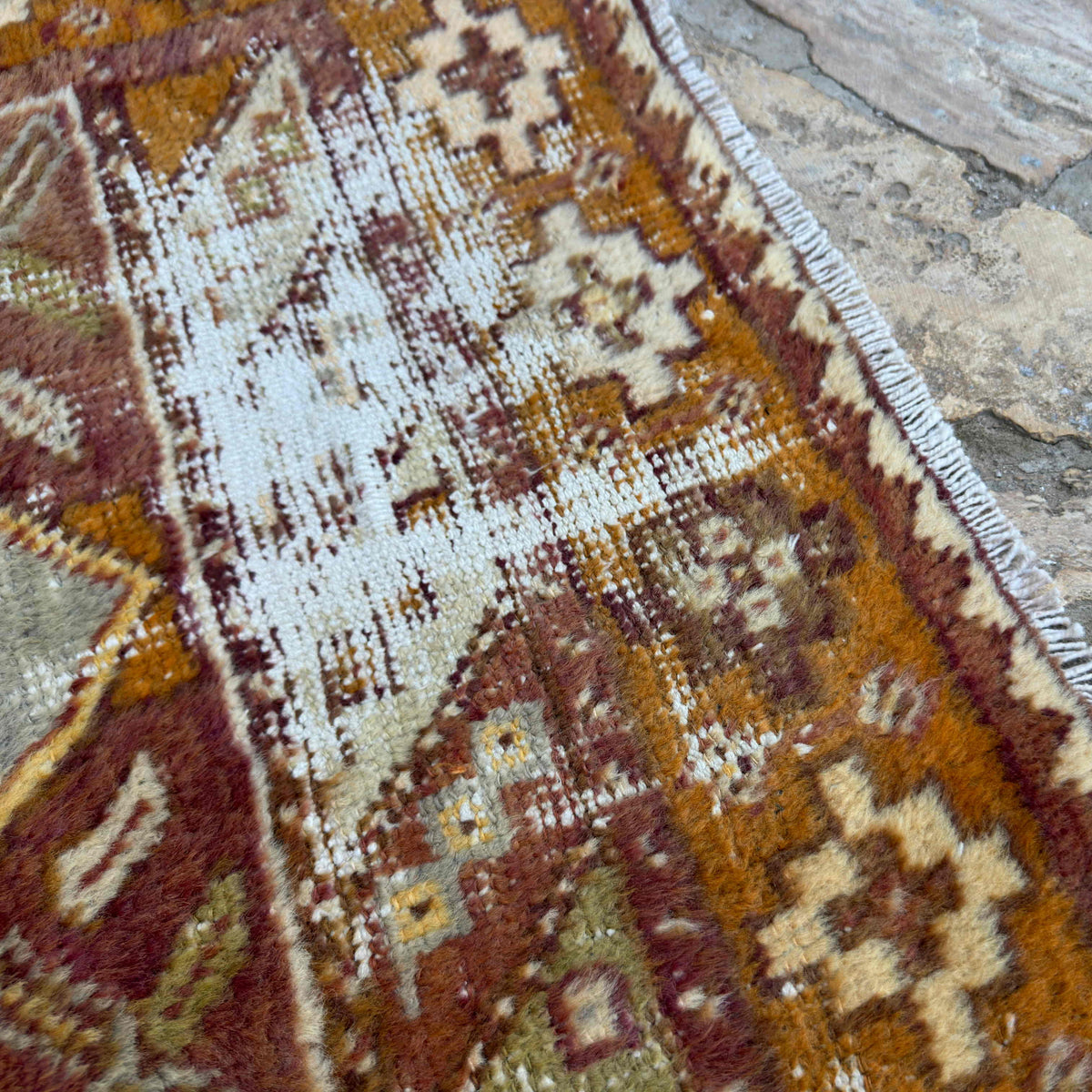 Close-up of the orange vintage Turkish distressed rug showing traditional details, hand-knotted weave, wool and cotton and low pile.