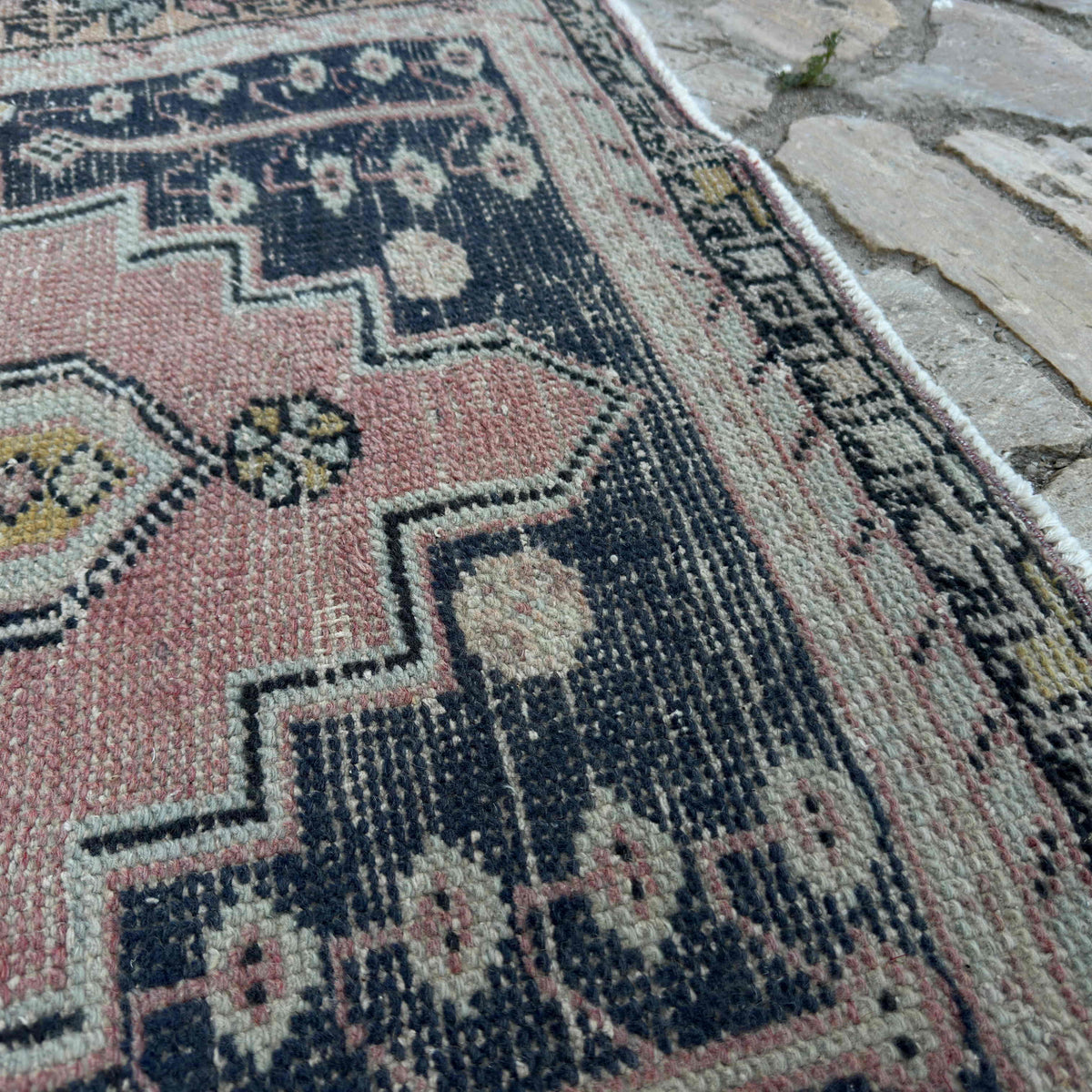 Close-up of the pink vintage Turkish distressed rug showing traditional details, hand-knotted weave, wool and cotton and low pile.