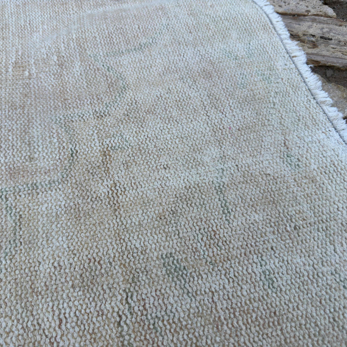 Close-up of the beige vintage Turkish distressed rug showing neutral details, hand-knotted weave, wool and cotton and low pile.
