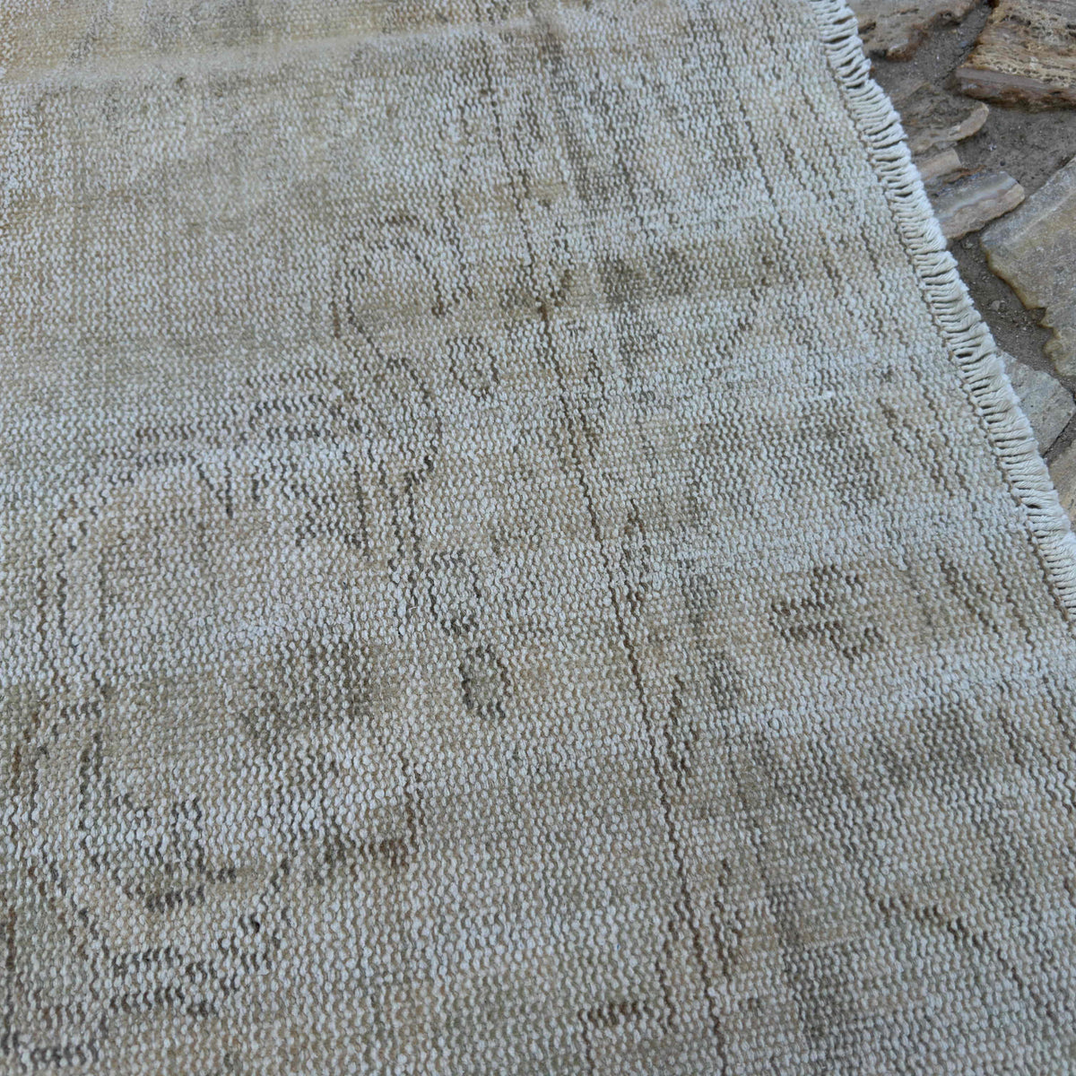 Close-up of the beige vintage Turkish distressed rug showing neutral details, hand-knotted weave, wool and cotton and low pile.