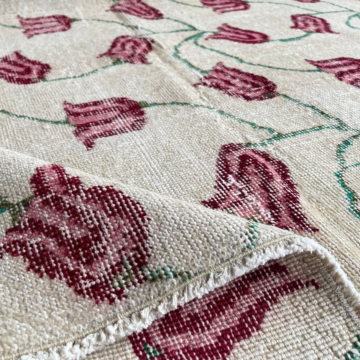Close-up of the beige vintage Turkish distressed rug showing floral details, hand-knotted weave, wool and cotton and low pile.