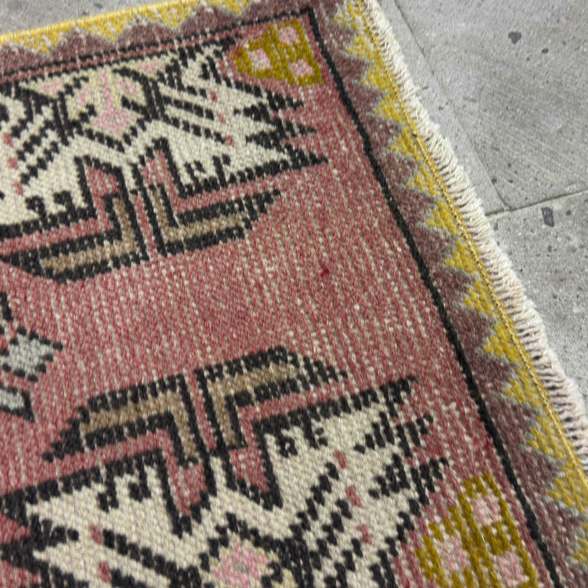 Close-up of the pink vintage Turkish geometric carpet showing traditional details, hand-knotted weave, wool and cotton and low pile.