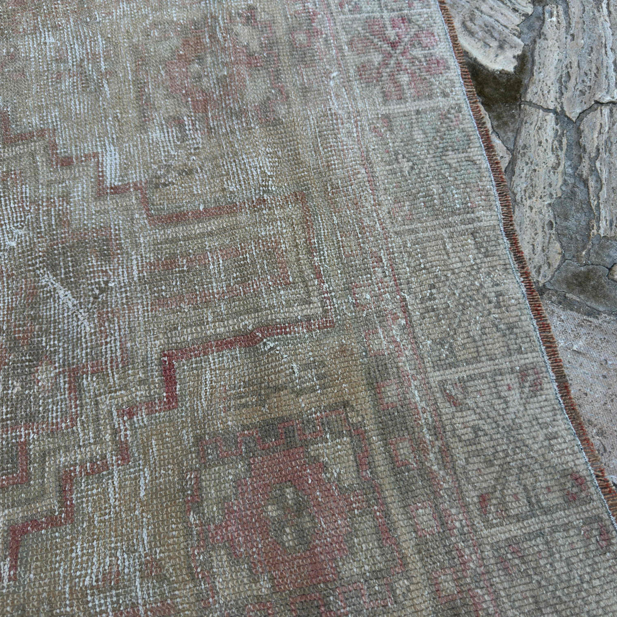 Close-up of the pale red vintage Turkish oriental rug showing neutral details, hand-knotted weave, wool and cotton and low pile.