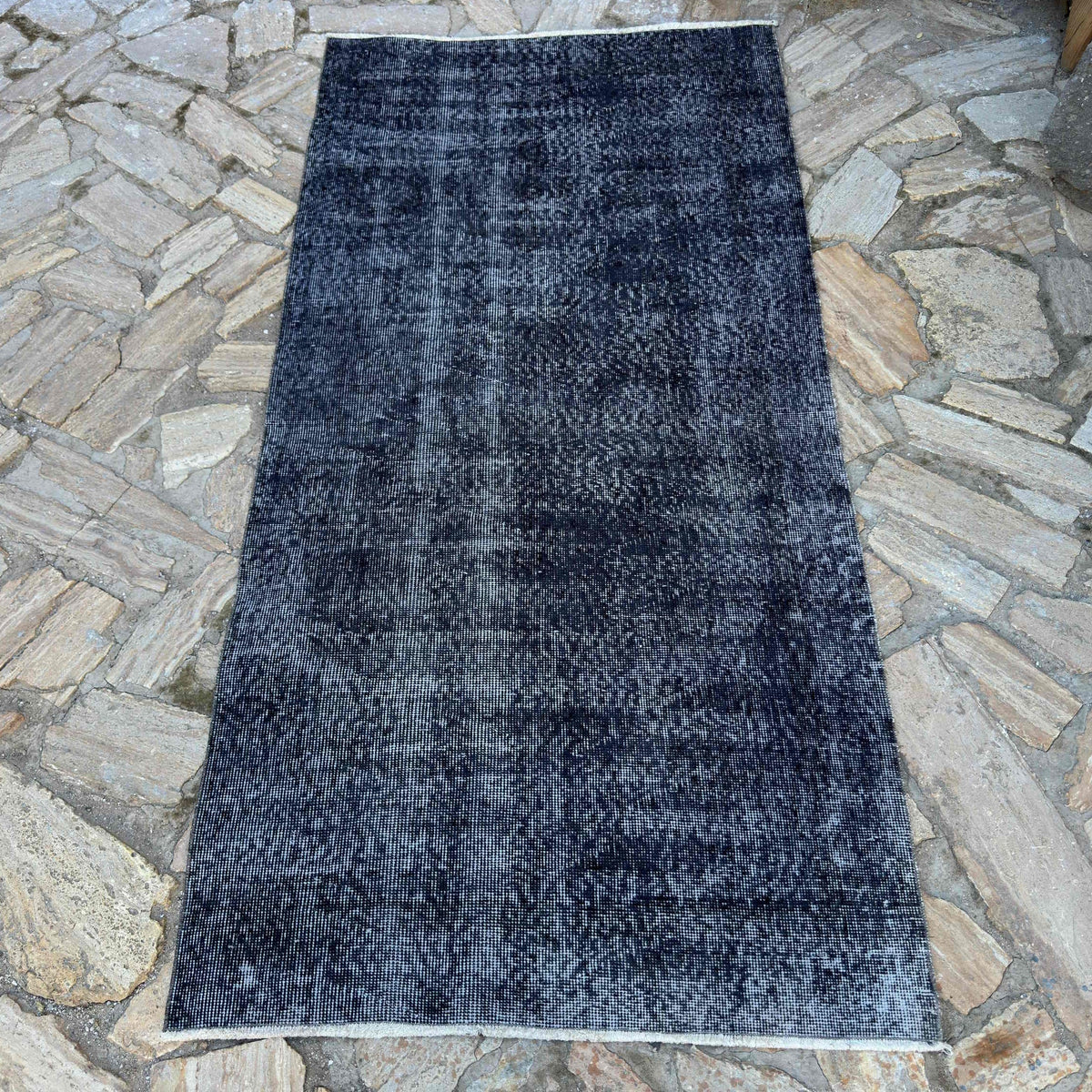 Black 3' x 7' vintage Turkish overdyed rug in wool and cotton, shown on the floor.