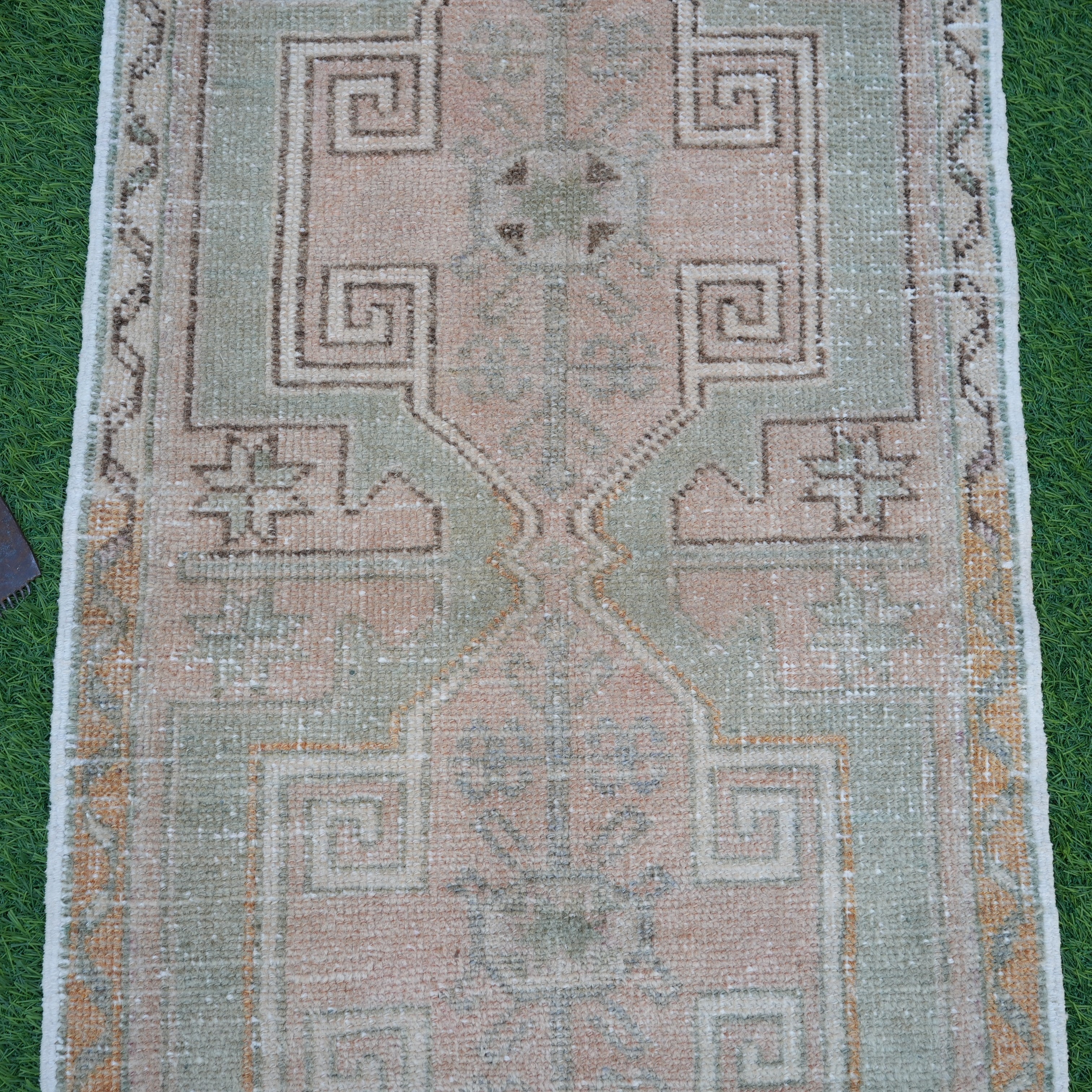 Close-up of the pink vintage Turkish small rug showing neutral details, hand-knotted weave, wool and cotton and low pile.