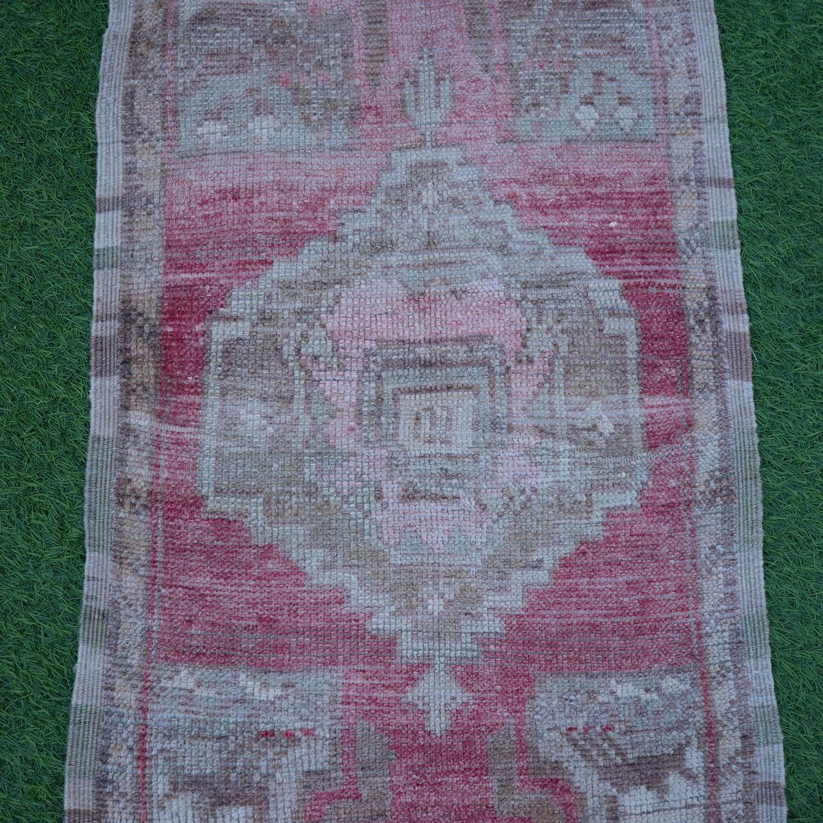 Close-up of the pale red vintage turkish rug showing geometric details, hand-knotted weave, wool and cotton and low pile.