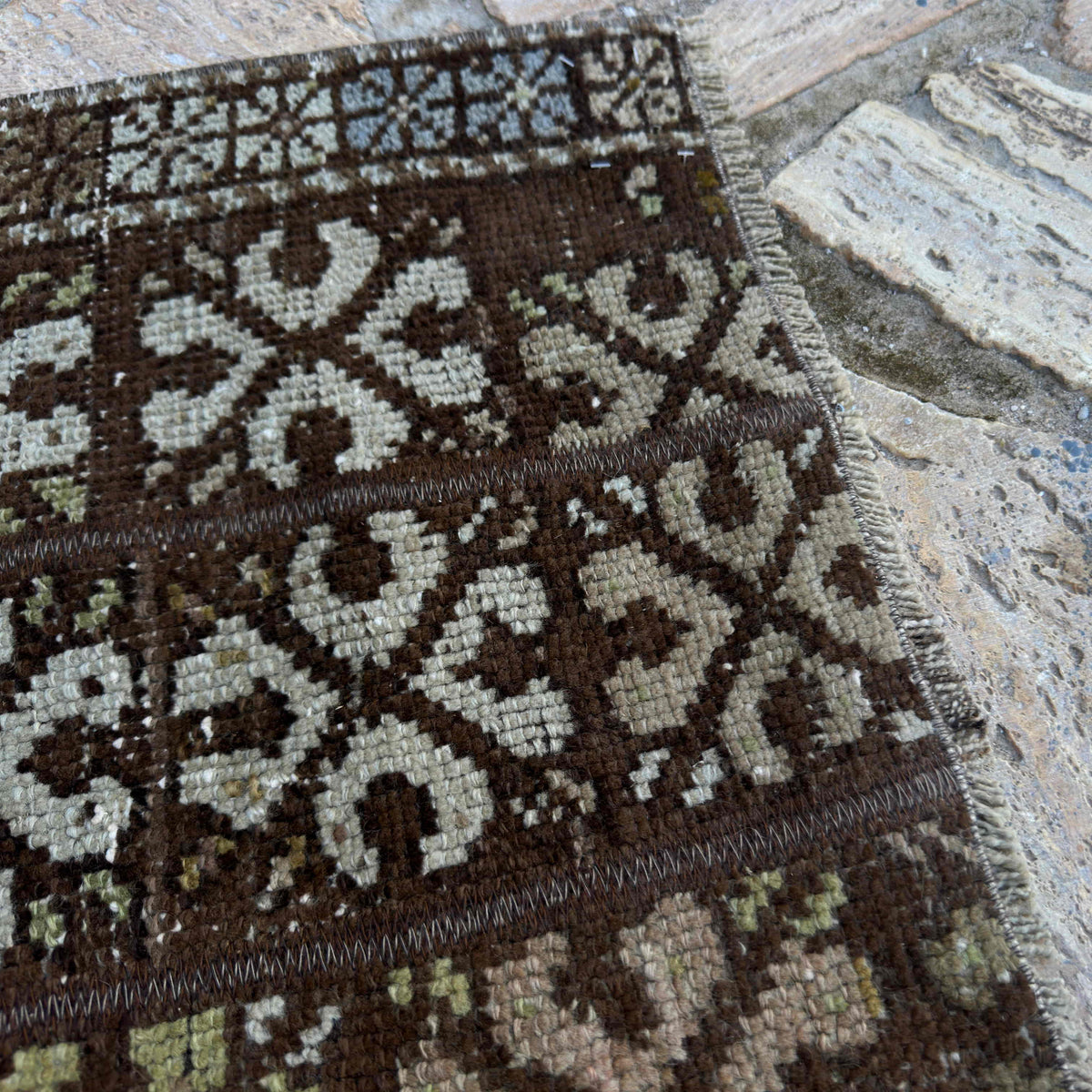Close-up of the brown vintage turkish rug showing patchwork details, hand-knotted weave, wool and cotton and low pile.