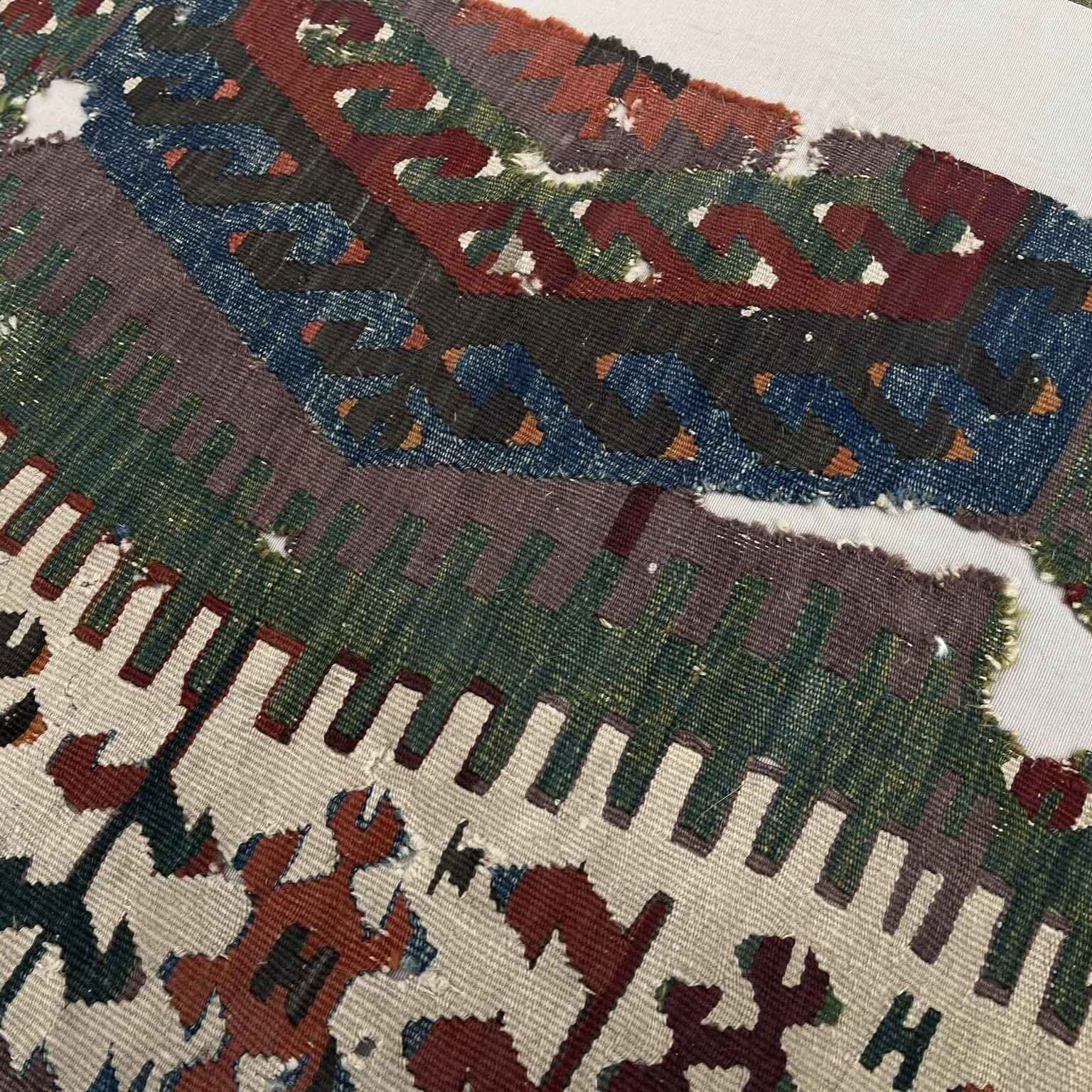 Macro close-up of an antique Anatolian kilim fragment showing hand-spun wool texture and natural dye patina in red, blue, green, and mustard tones