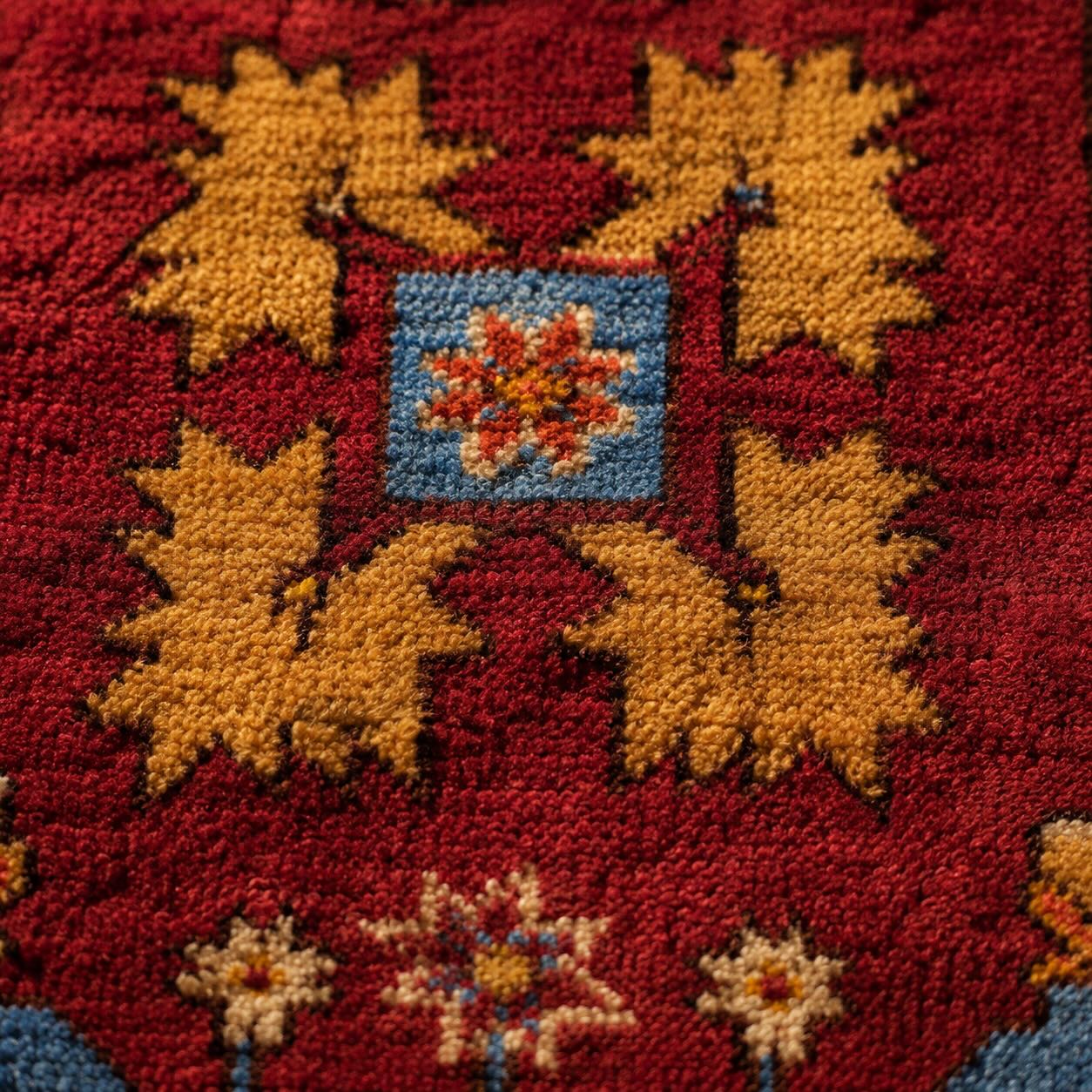 Extreme close-up of hand-knotted wool pile on an antique Gelveri rug, showing mustard-gold star motifs and a blue floral medallion against a deep red field
