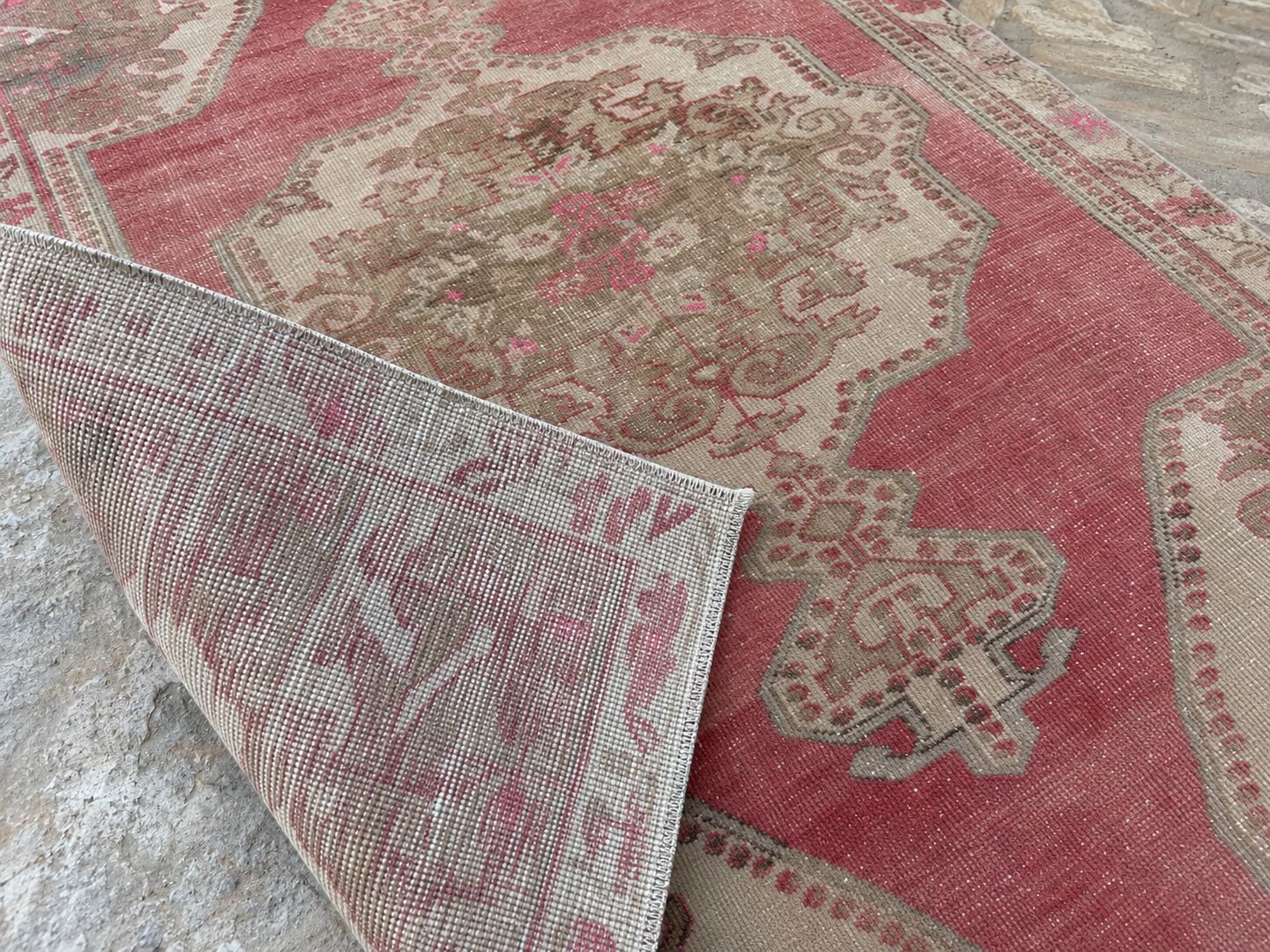 Close-up of a vintage red rug folded back to reveal hand-tied knots and natural abrash color variation