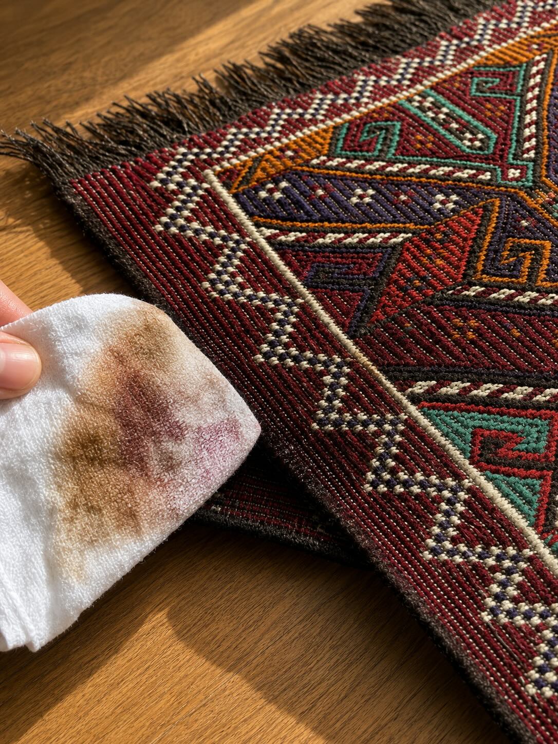 Hand testing a hidden corner of a handwoven kilim rug with a damp white cloth before cleaning