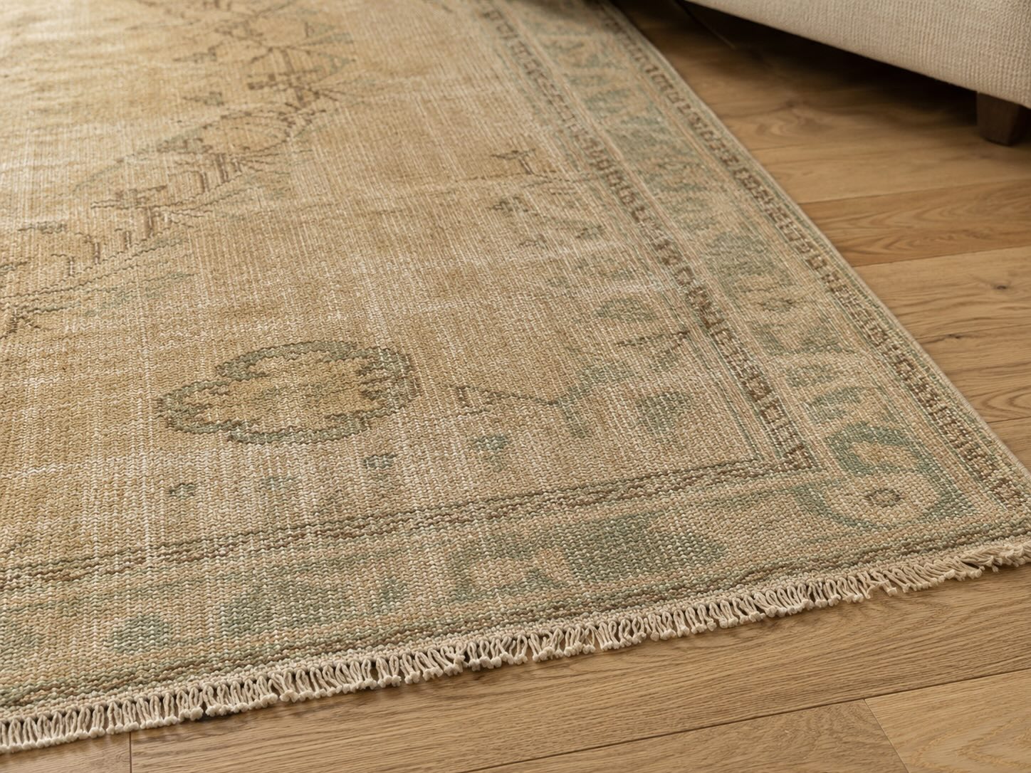 Close-up of the Winslow vintage hand-knotted Turkish rug showing natural wool texture, abrash color variation, and hand-finished fringe beside a beige couch.
