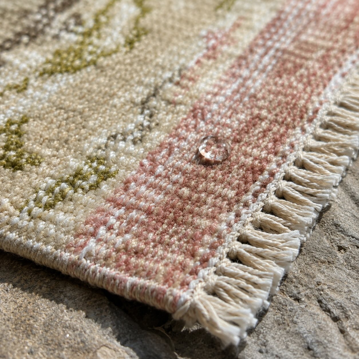 Macro close-up of a handknotted vintage runner's fringe and weave with a water droplet on the pile