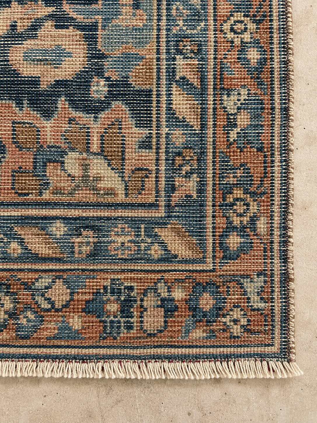 Close-up of the back corner of a hand-knotted vintage rug showing individual knots and the natural warp-thread fringe with no fabric backing