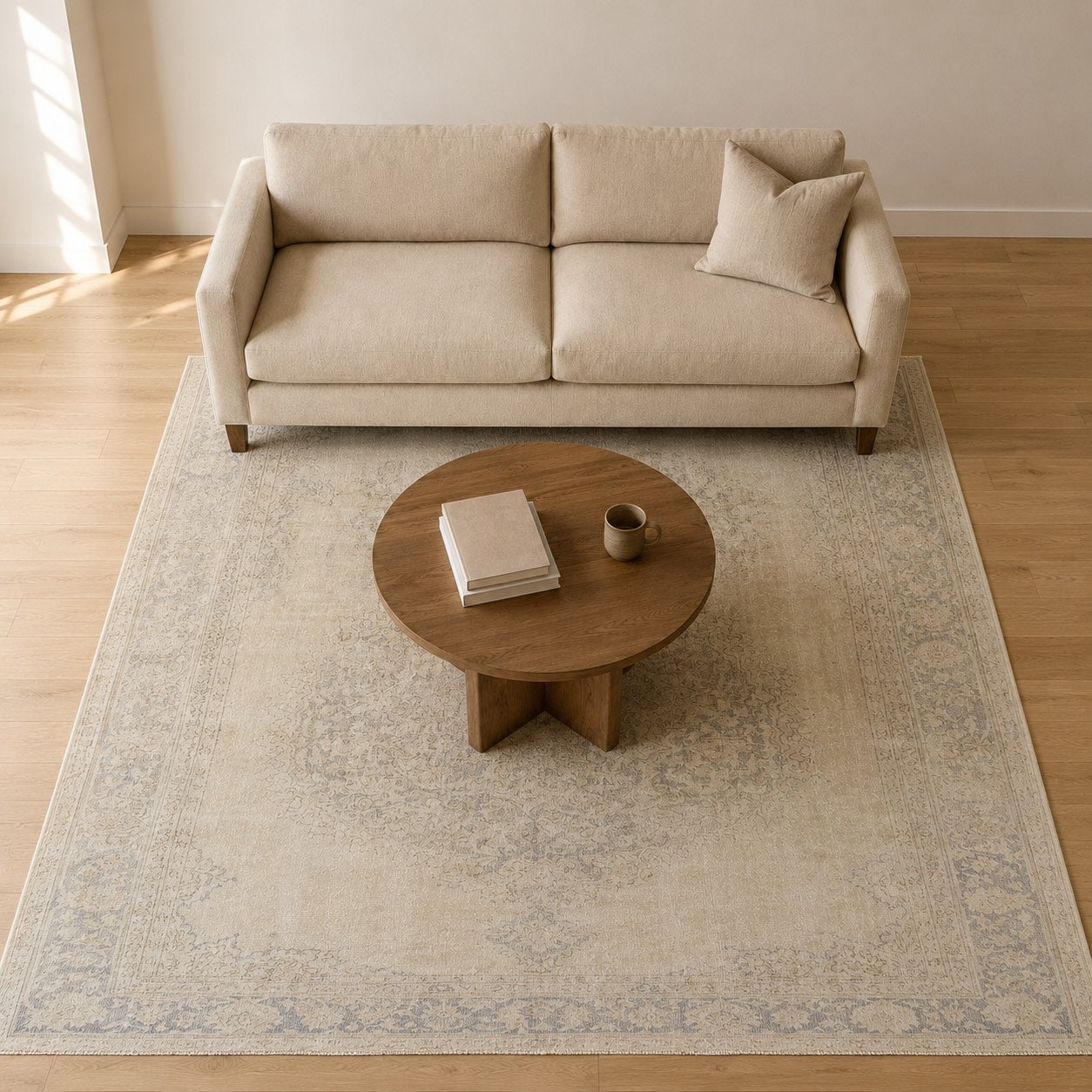 Overhead view of the Sincere vintage Persian-style beige and blue rug sized correctly under a beige sofa and round coffee table, illustrating proper rug sizing for a living room.