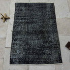 Black 2' x 3' Turkish mini overdyed rug in wool and cotton, shown on the floor.