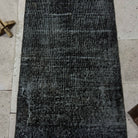 1970s black Turkish mini runner rug with overdyed design, hand-knotted weave and low pile.