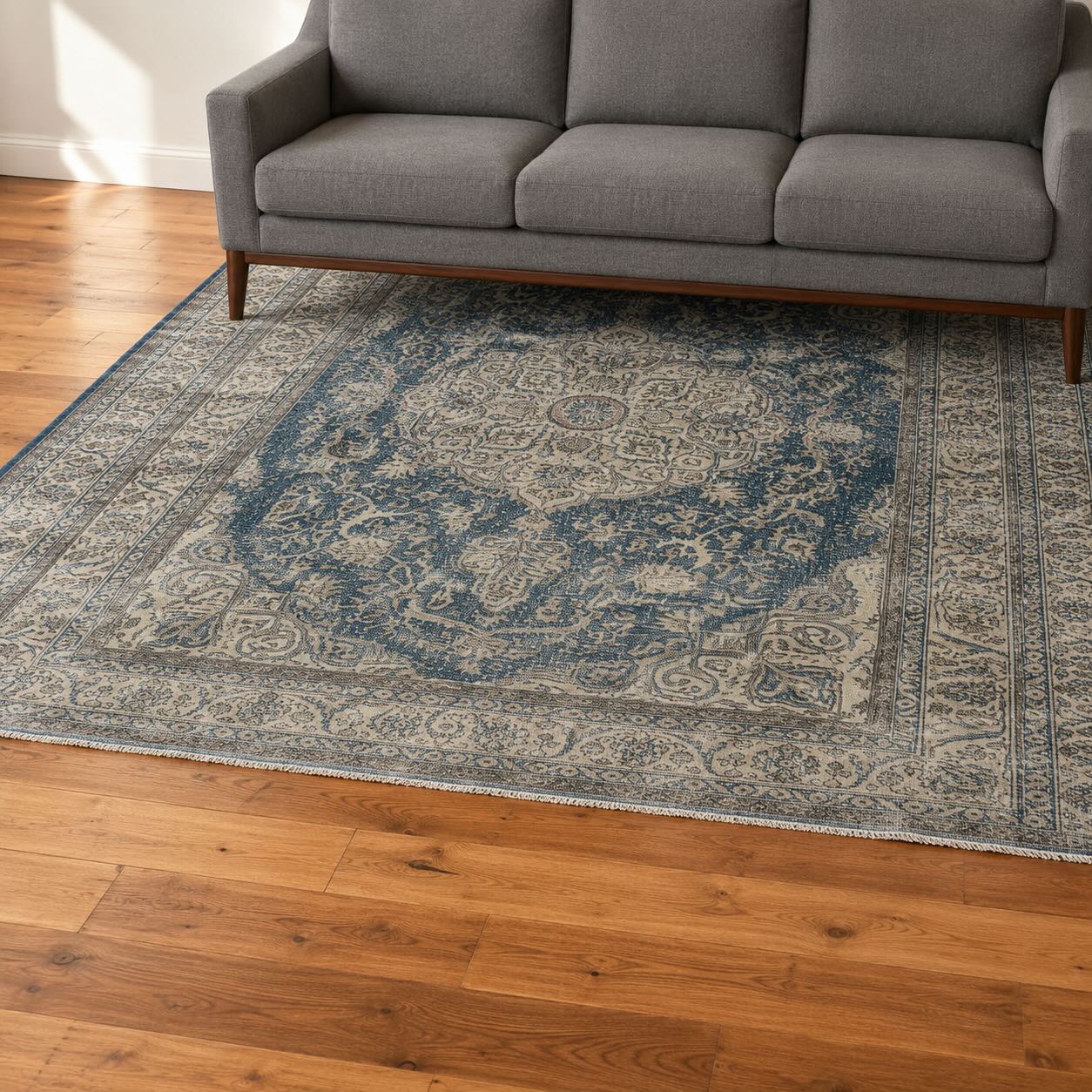 Navy blue vintage medallion rug against a warm wood floor beneath a gray sofa, showing floor and rug color contrast