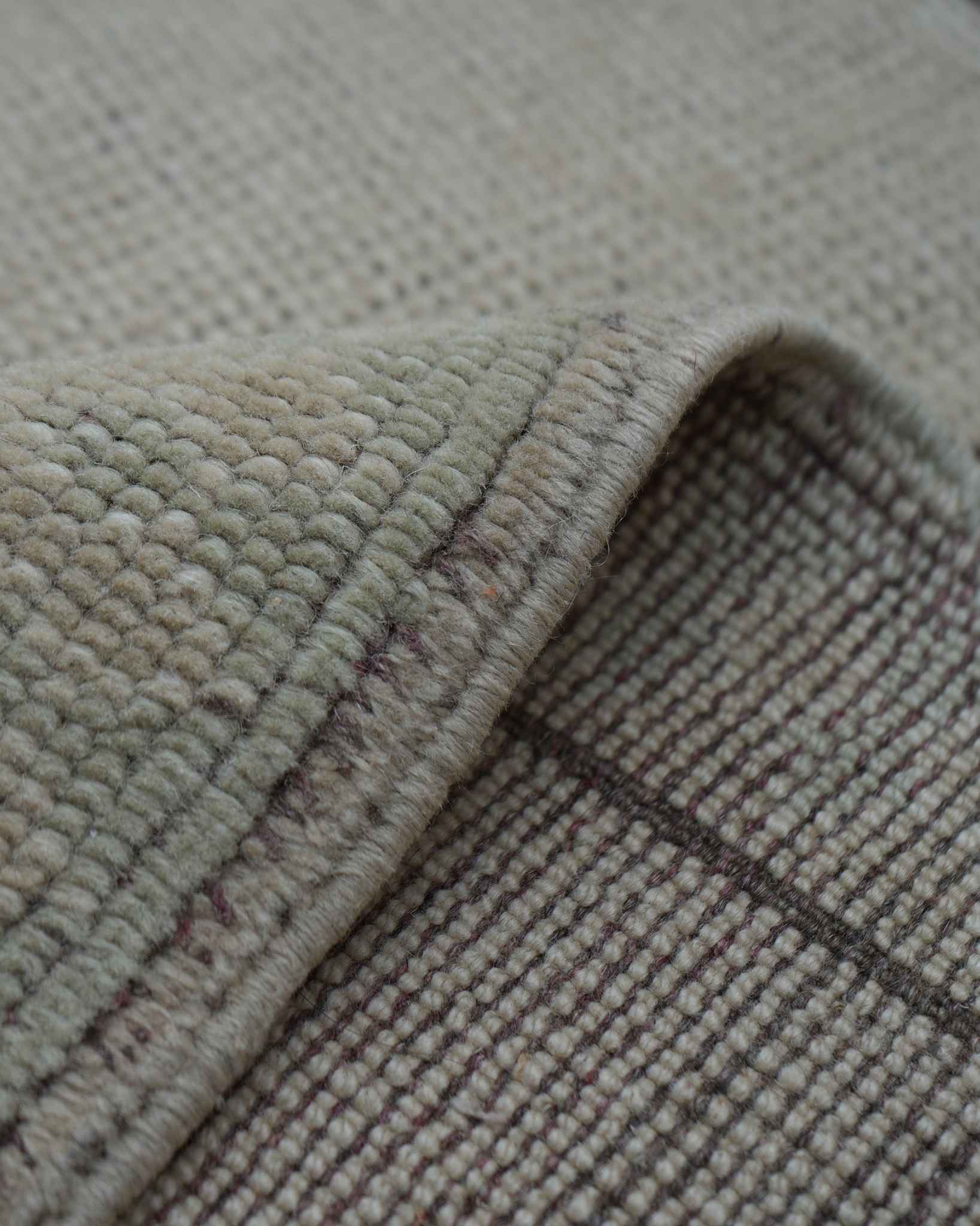 Back of a hand-knotted rug with one corner folded over, showing knot structure and foundation threads