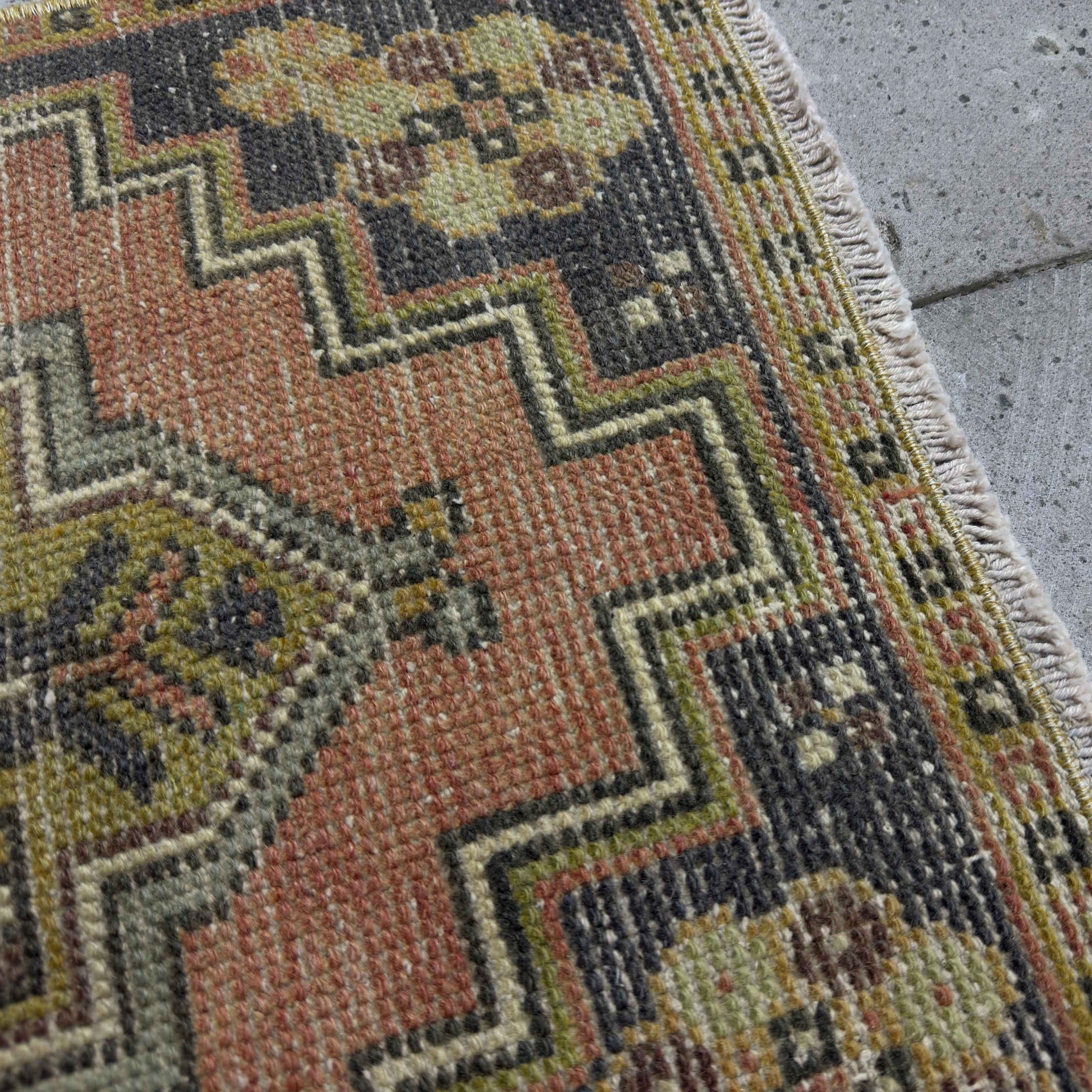 Close-up of the pale red Turkish small vintage distressed rug showing traditional details, hand-knotted weave, wool and cotton and low pile.