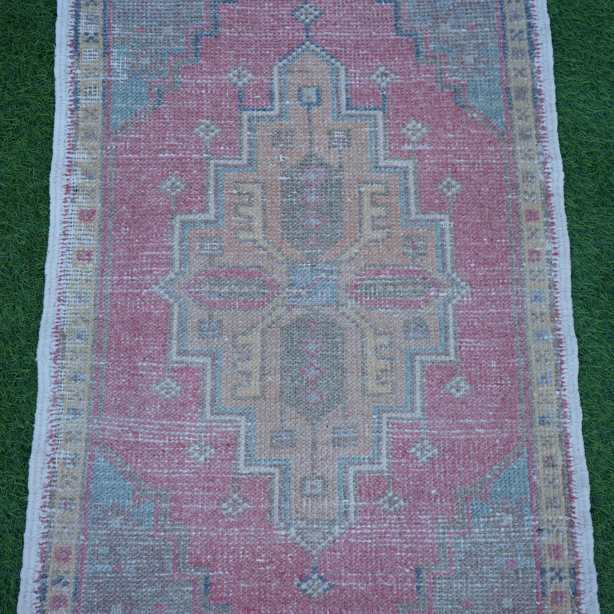 Close-up of the pink Turkish small vintage rug showing traditional details, hand-knotted weave, wool and cotton and low pile.
