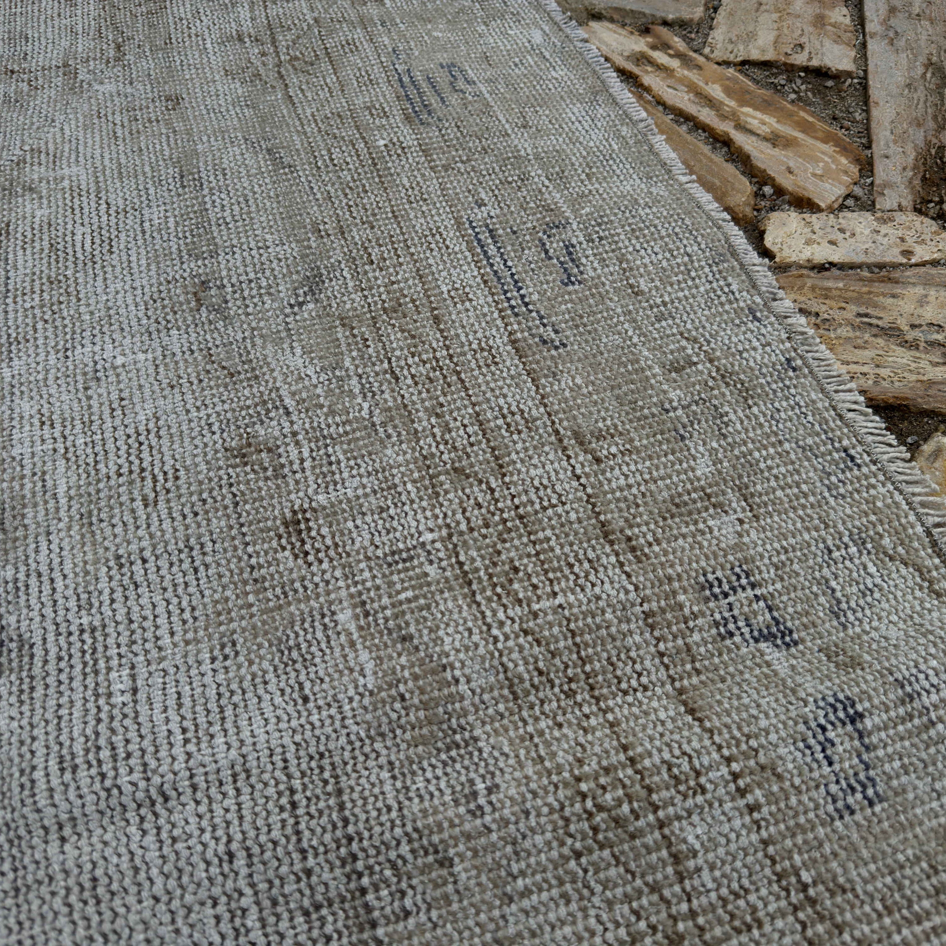 Close-up of the pale gray vintage Turkish distressed carpet showing neutral details, hand-knotted weave, wool and cotton and low pile.