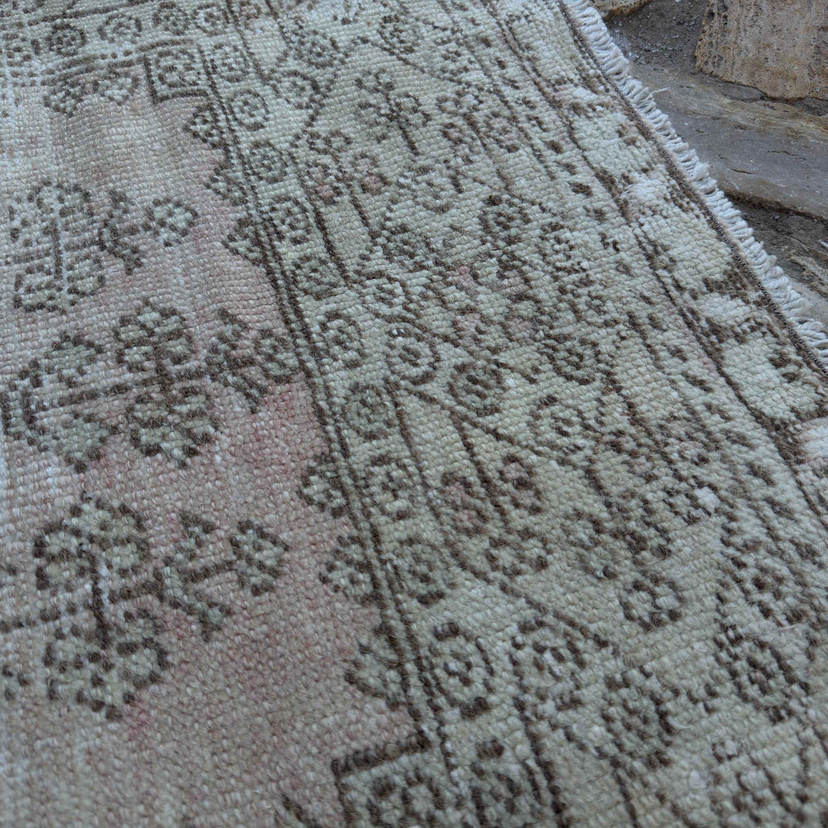 Close-up of the pale pink vintage Turkish distressed rug showing neutral details, hand-knotted weave, wool and cotton and low pile.