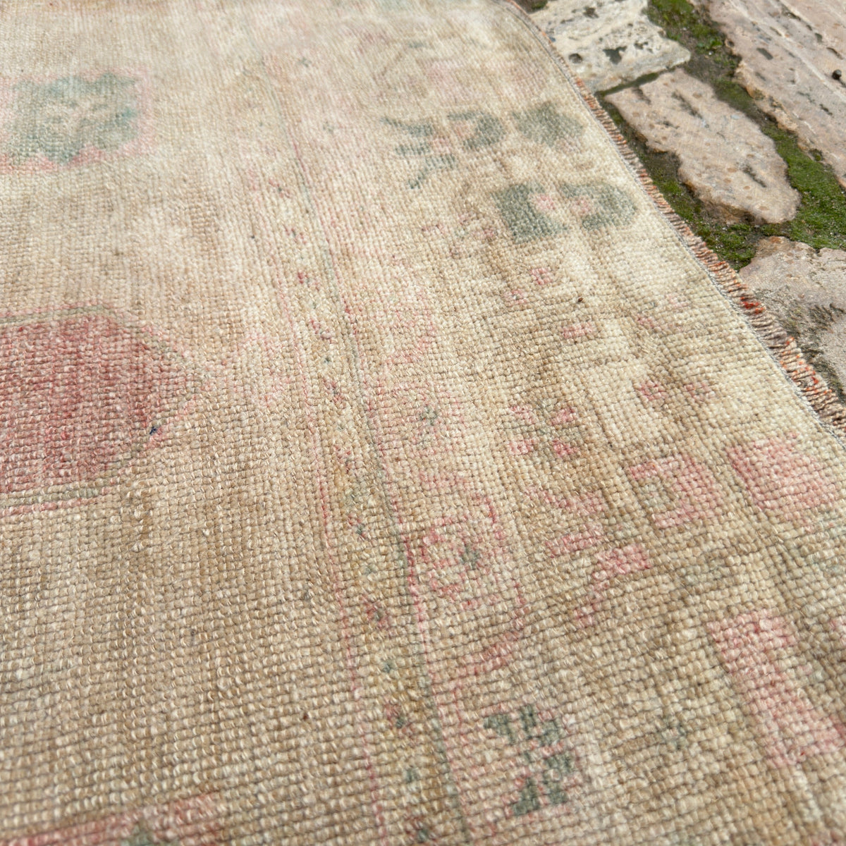 Close-up of the beige vintage Turkish distressed rug showing medallion details, hand-knotted weave, wool and cotton and low pile.