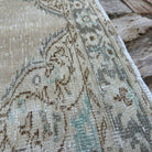 Close-up of the beige vintage Turkish distressed rug showing medallion details, hand-knotted weave, wool and cotton and low pile.