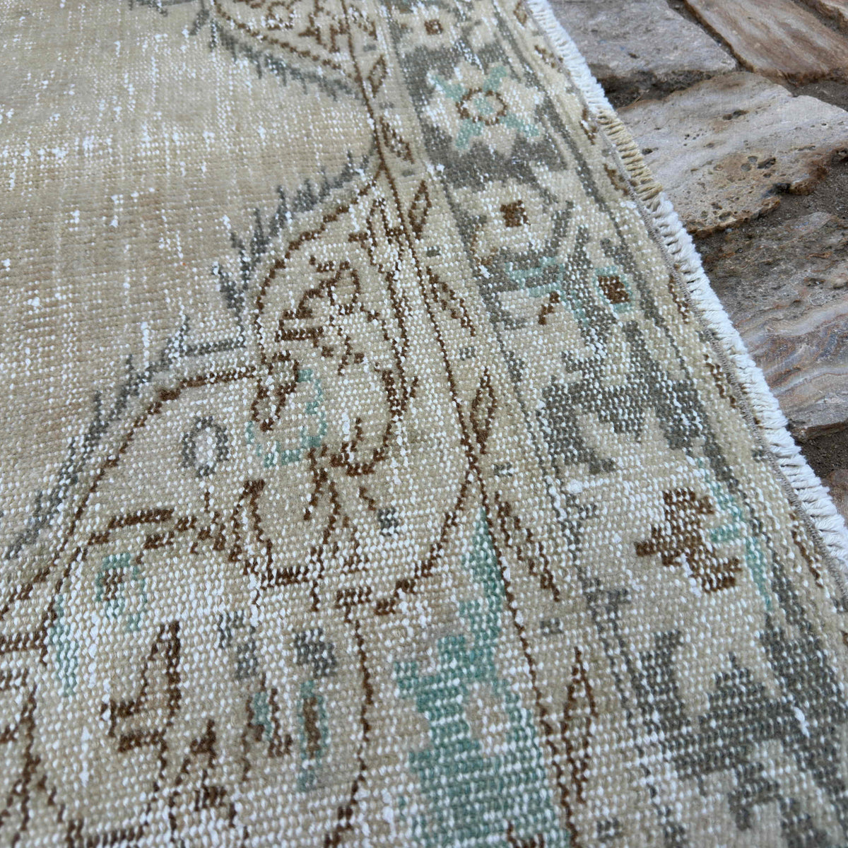 Close-up of the beige vintage Turkish distressed rug showing medallion details, hand-knotted weave, wool and cotton and low pile.