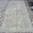 Beige 5' x 9' vintage Turkish distressed rug in wool and cotton, shown on the floor.