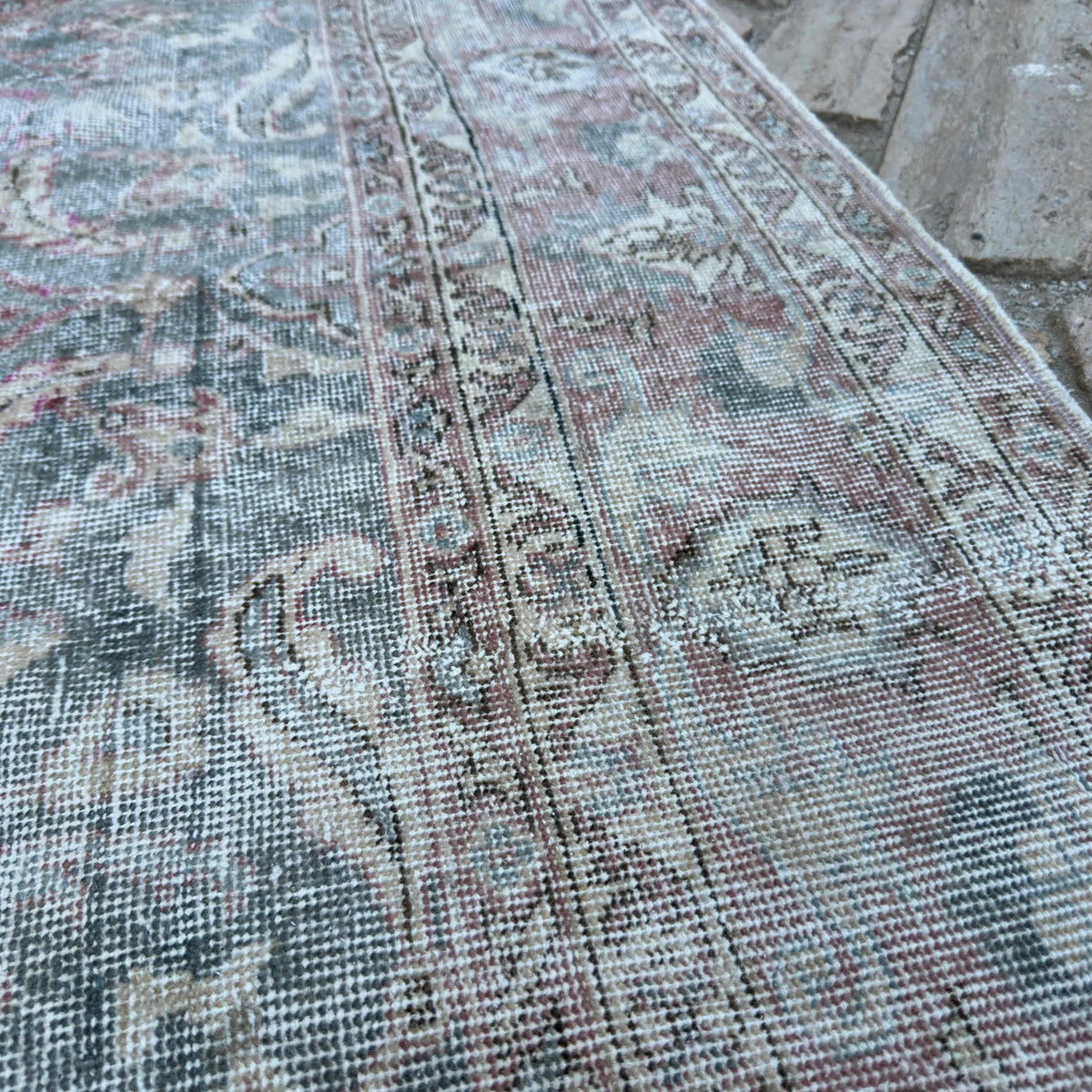 Close-up of the pale green vintage Turkish distressed rug showing traditional details, hand-knotted weave, wool and cotton and low pile.