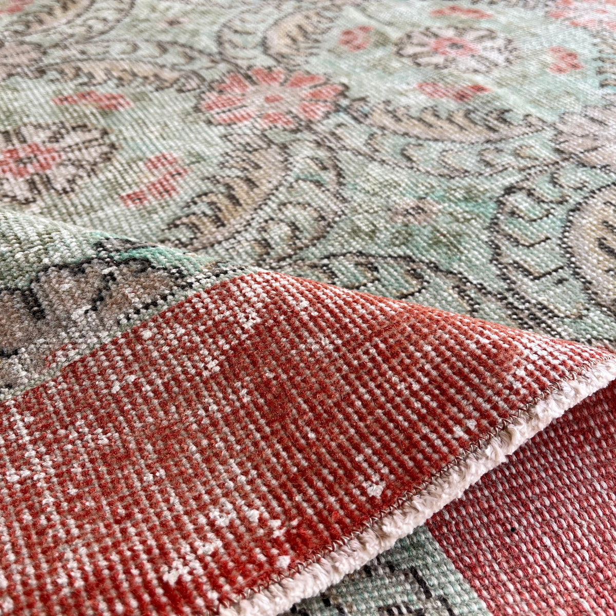 Close-up of the pale green vintage Turkish floral rug showing floral details, hand-knotted weave, wool and cotton and low pile.