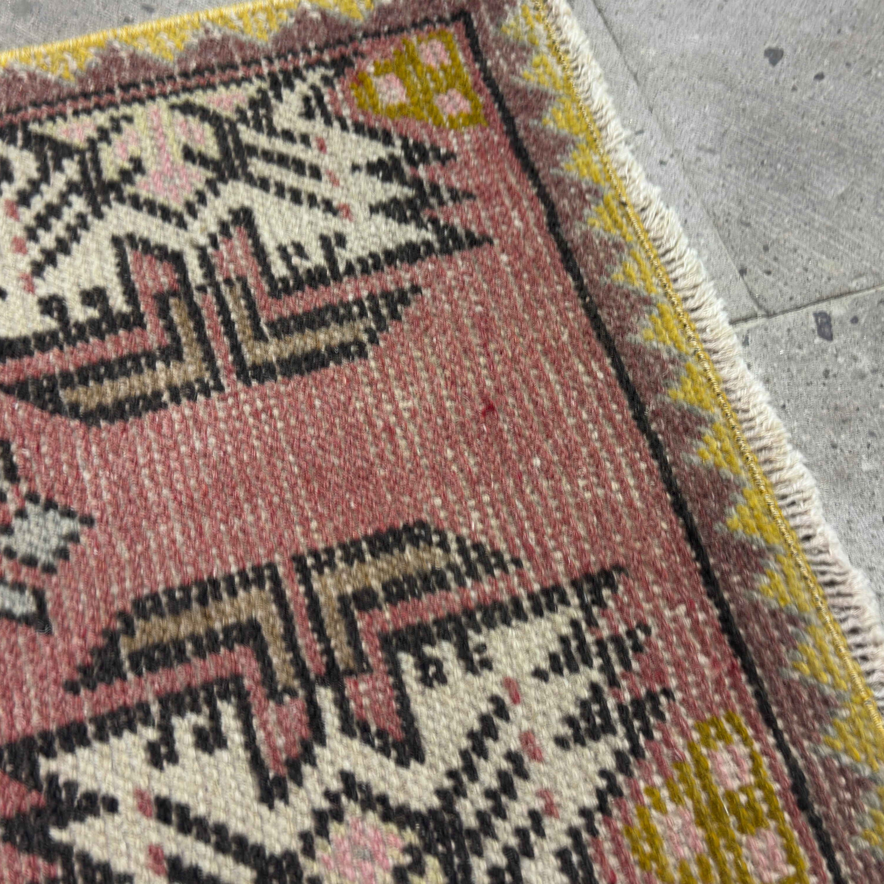 Close-up of the pink vintage Turkish geometric carpet showing traditional details, hand-knotted weave, wool and cotton and low pile.