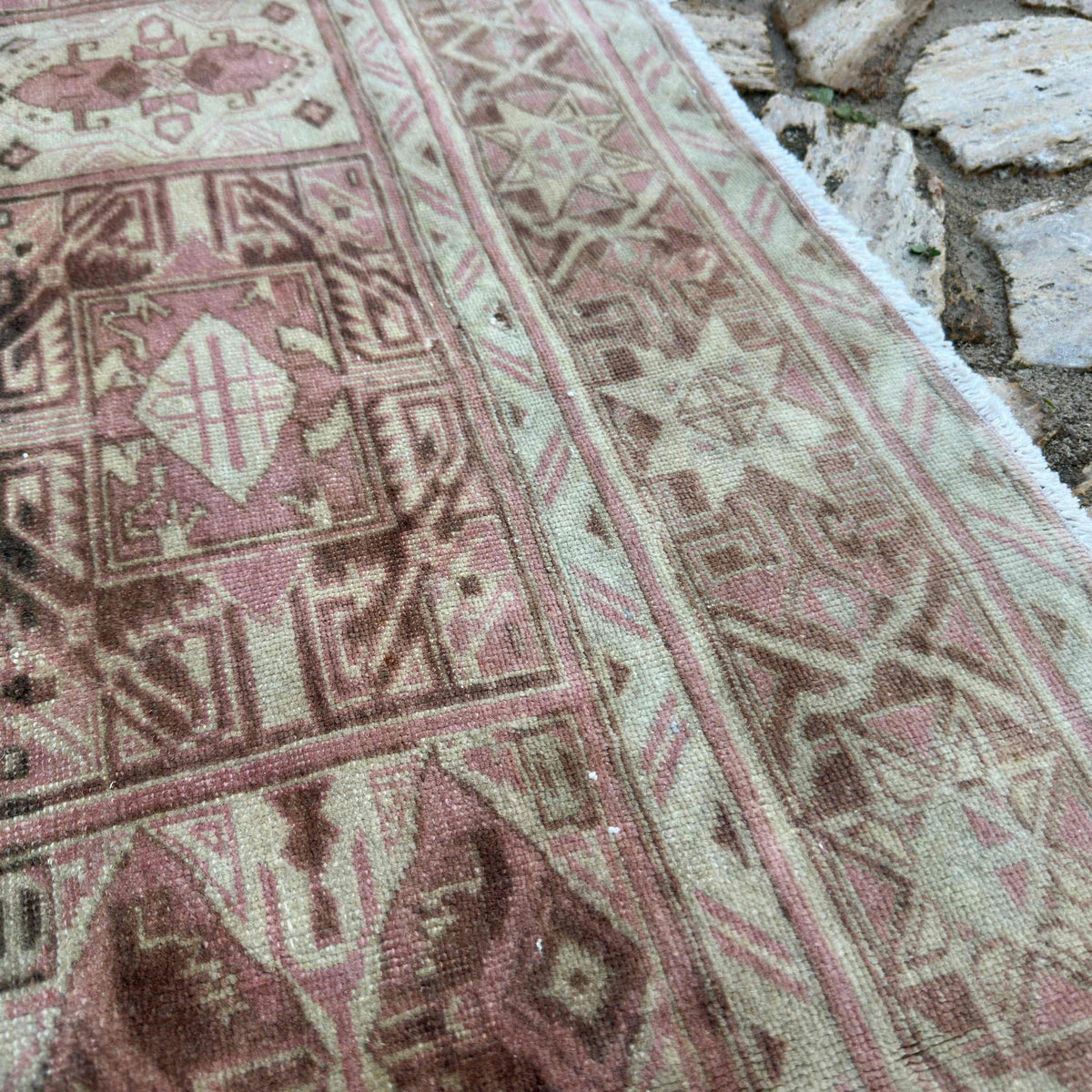 Close-up of the pink vintage Turkish geometric rug showing neutral details, hand-knotted weave, wool and cotton and low pile.
