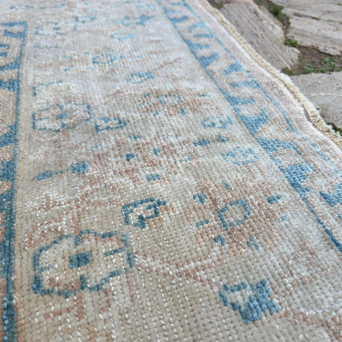 Close-up of the pink vintage Turkish oushak rug showing neutral details, hand-knotted weave, wool and cotton and low pile.