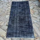 Black 3' x 7' vintage Turkish overdyed rug in wool and cotton, shown on the floor.