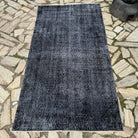 Black 4' x 7' vintage Turkish overdyed rug in wool and cotton, shown on the floor.