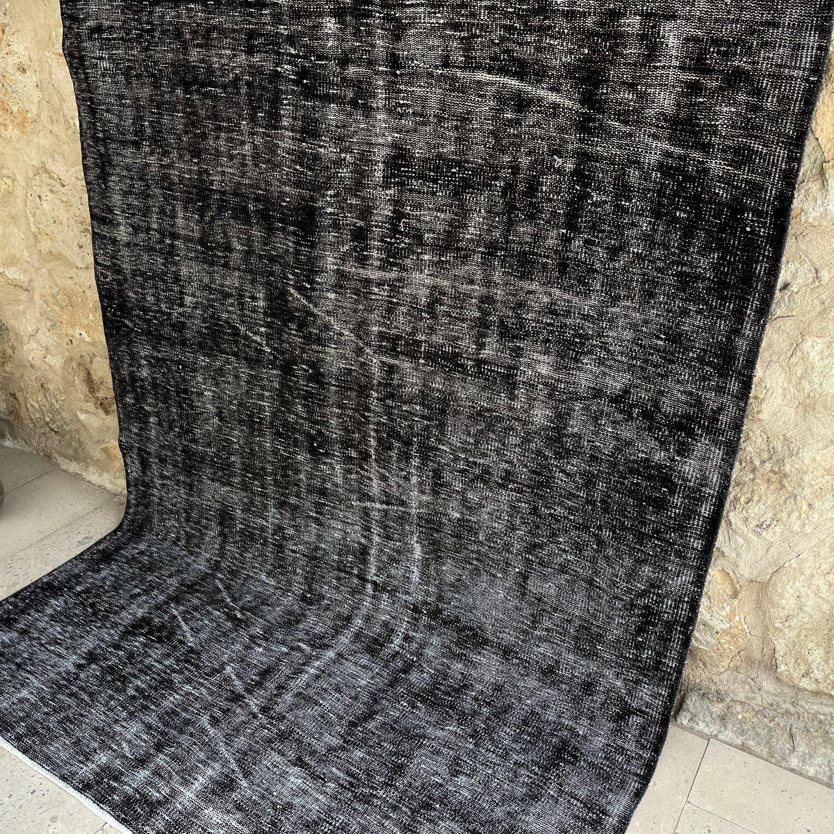Black 5' x 9' vintage Turkish overdyed rug in wool and cotton, shown on the floor.