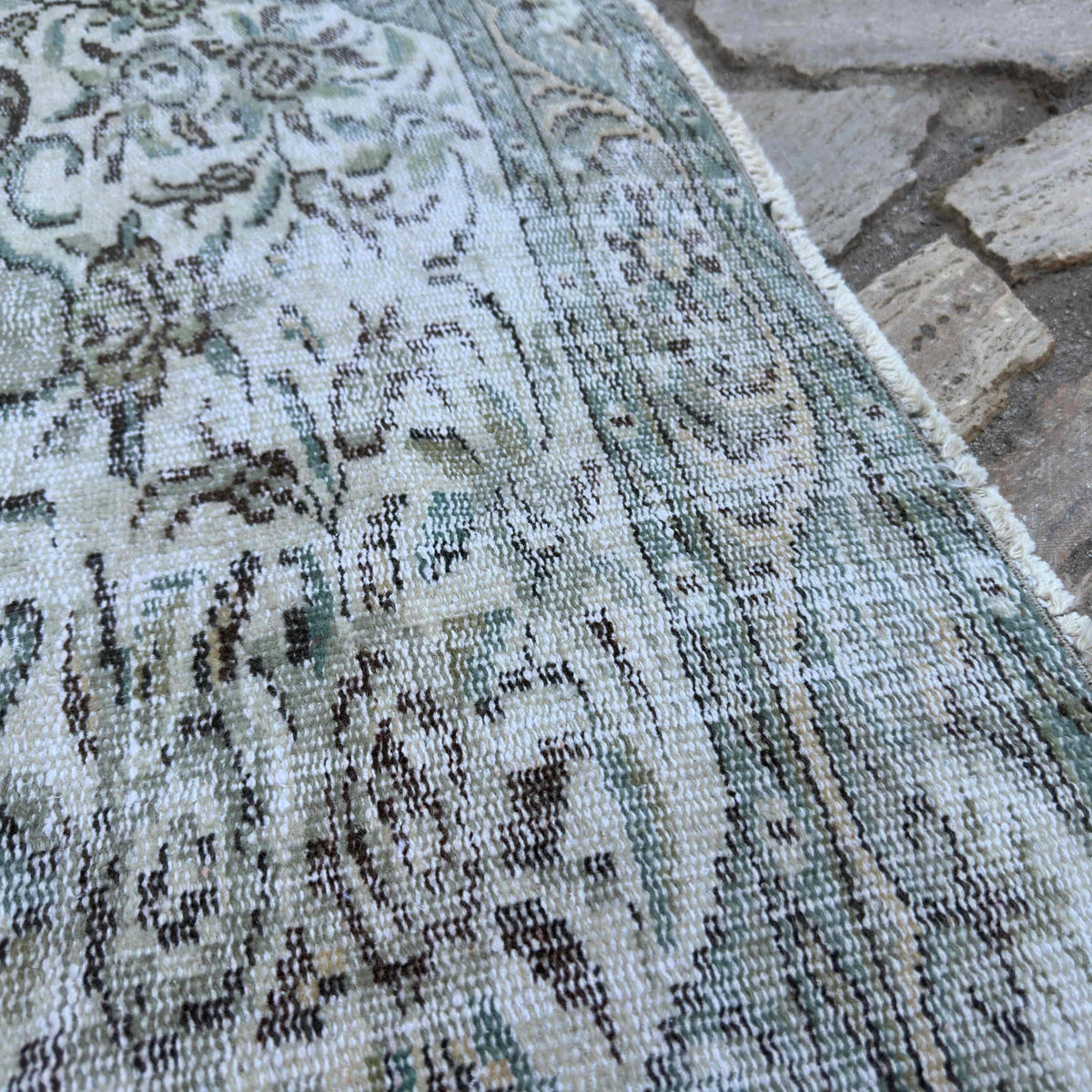 Close-up of the green vintage Turkish persian style rug showing geometric details, hand-knotted weave, wool and cotton and low pile.