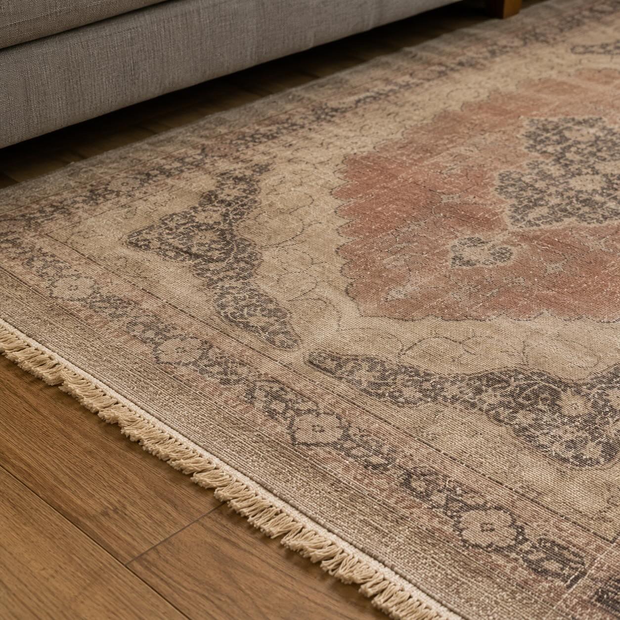 Close-up of a vintage terracotta and beige medallion rug showing hand-knotted texture, natural color variation, and fringe detail next to a gray sofa