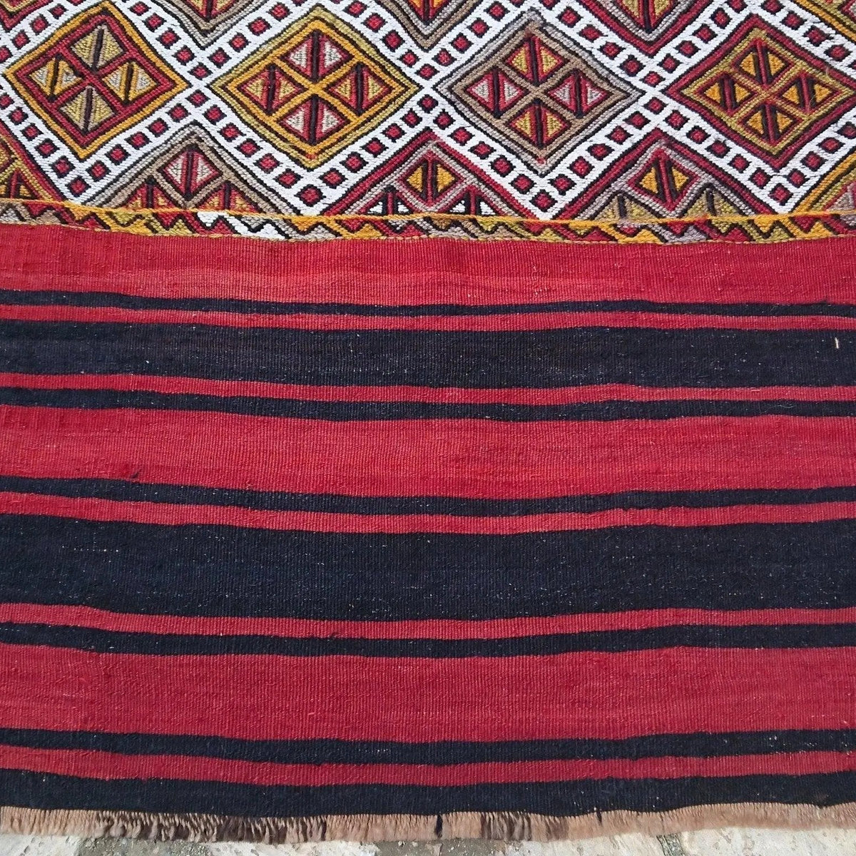 Close-up of the red vintage Turkish tribal kilim rug showing striped details, flatweave construction, wool and cotton and low pile.