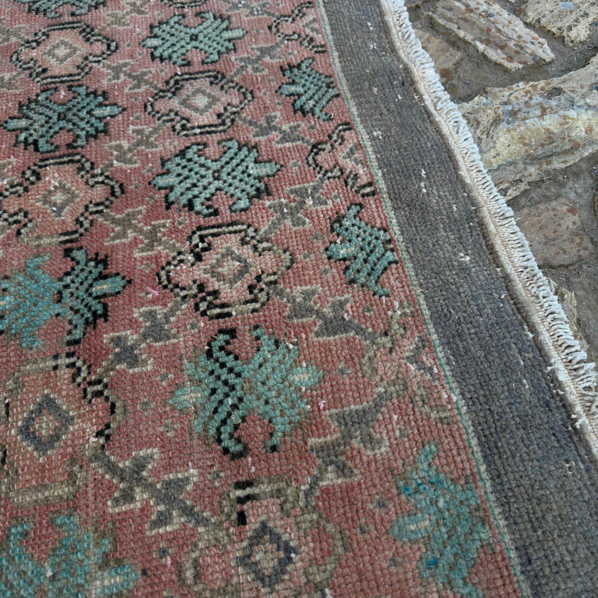 Close-up of the pale red vintage turkish rug showing floral details, hand-knotted weave, wool and cotton and low pile.