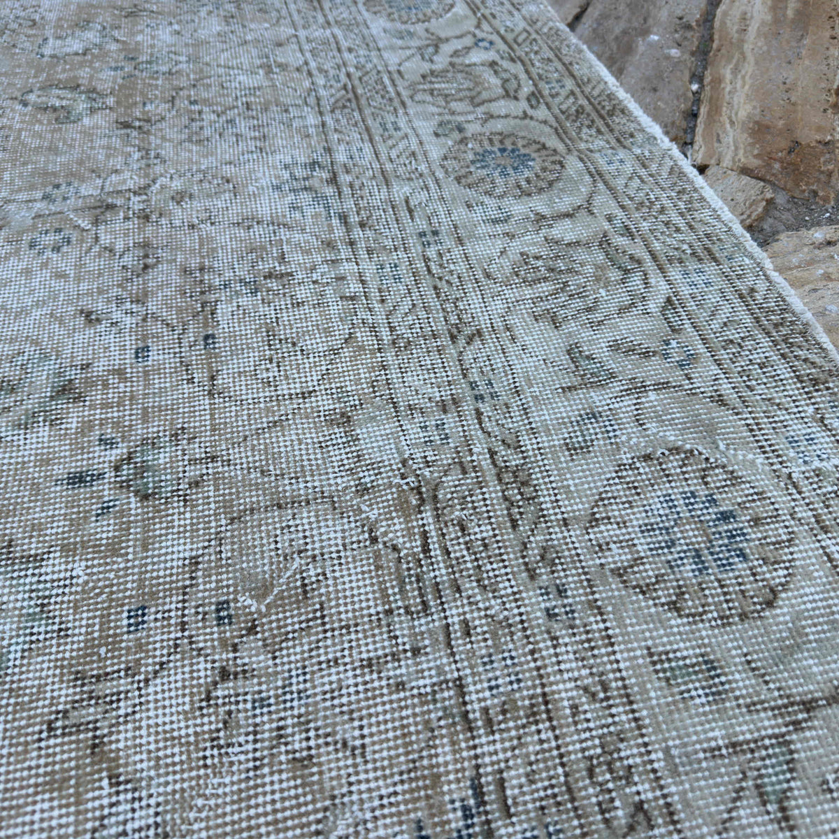 Close-up of the beige vintage turkish rug showing floral details, hand-knotted weave, wool and cotton and low pile.